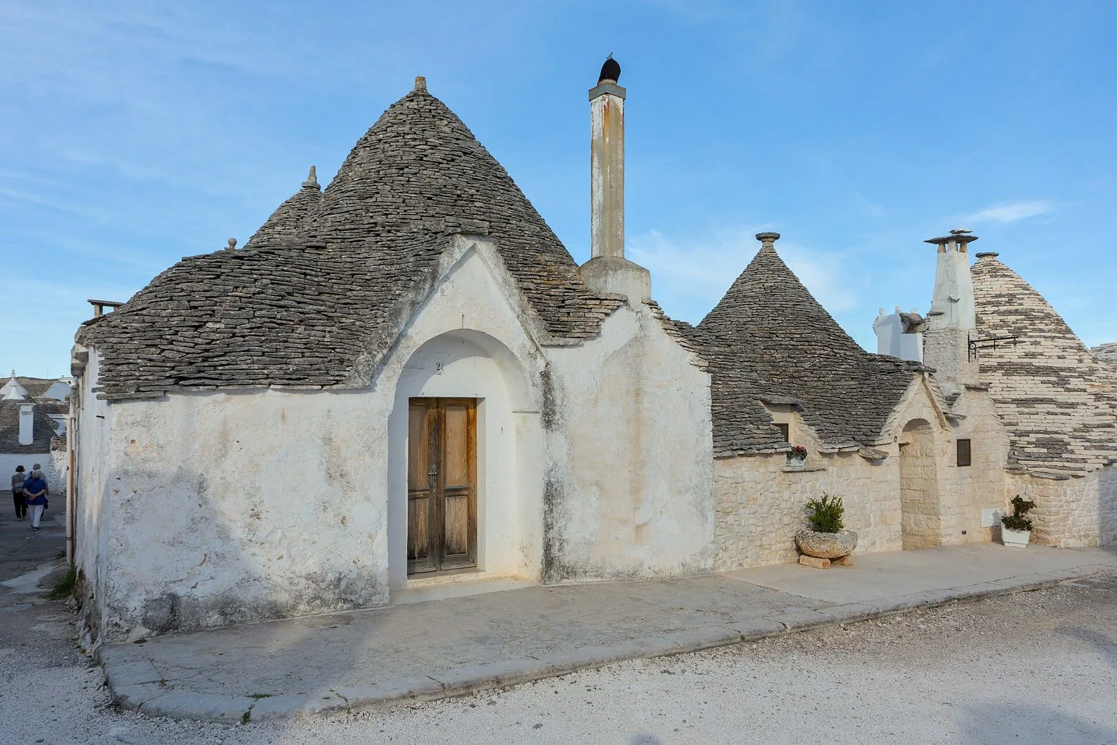 Trulli imbiancati a calce con tetti conici in pietra grigia lungo una strada del Rione Aia Piccola ad Alberobello