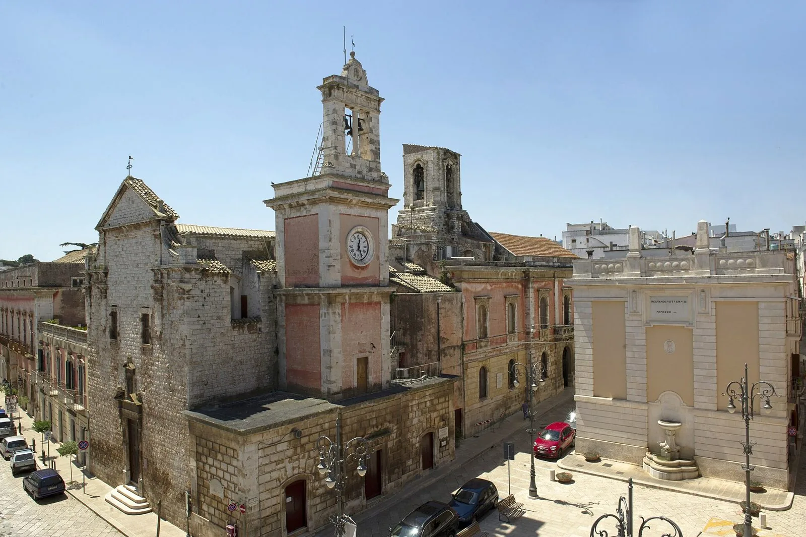 La chiesa di San Francesco con la torre dell'orologio e il Palazzo Municipale nel centro di Castellana Grotte, sotto un cielo azzurro