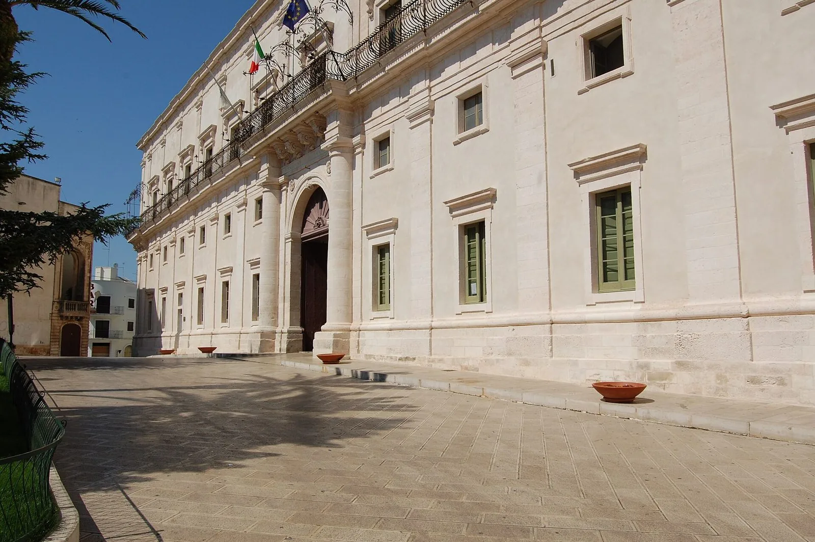 La facciata chiara del Palazzo Ducale di Martina Franca con il portale ad arco, il lungo balcone in ferro battuto e la piazza lastricata in una giornata di sole